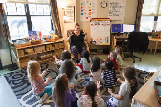 Student teacher sitting in a chair teaching small children