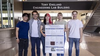 Seniors Kenny Conuel Oralde, Emmet Reamer, Rosa Carapia, Nicole Kormos and Micah Hagedorn stand in front of a research poster in the atrium of a campus building. 